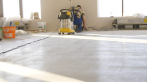 Workers in uniform cleaning room with a vacuum cleaner after installing wood parquet board during flooring work. Man vacuuming floor during repairs